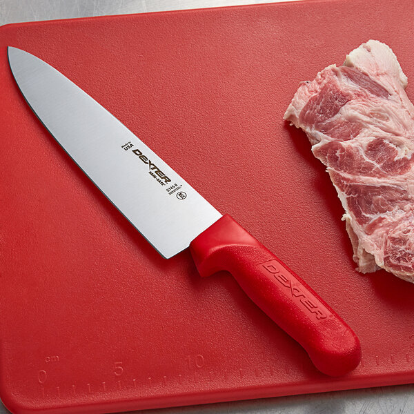 A Dexter-Russell chef knife with a red handle on a cutting board with meat.