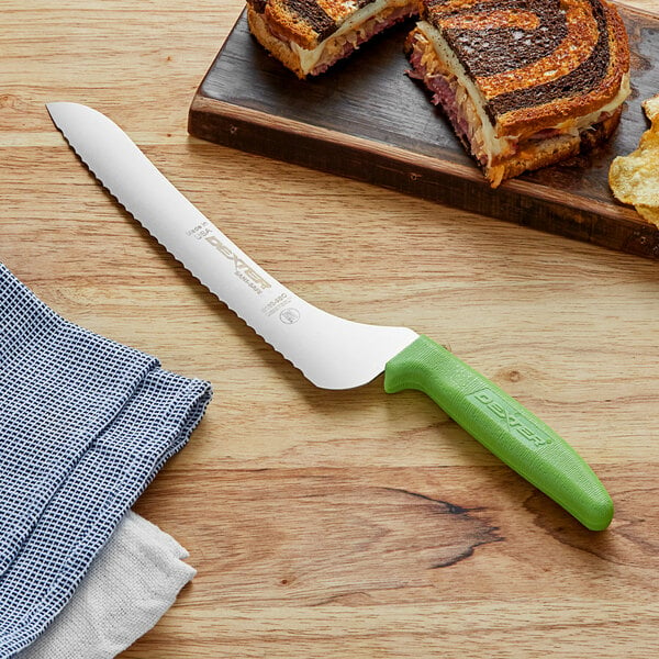 A Dexter-Russell bread knife with a green handle on a cutting board next to a sandwich.