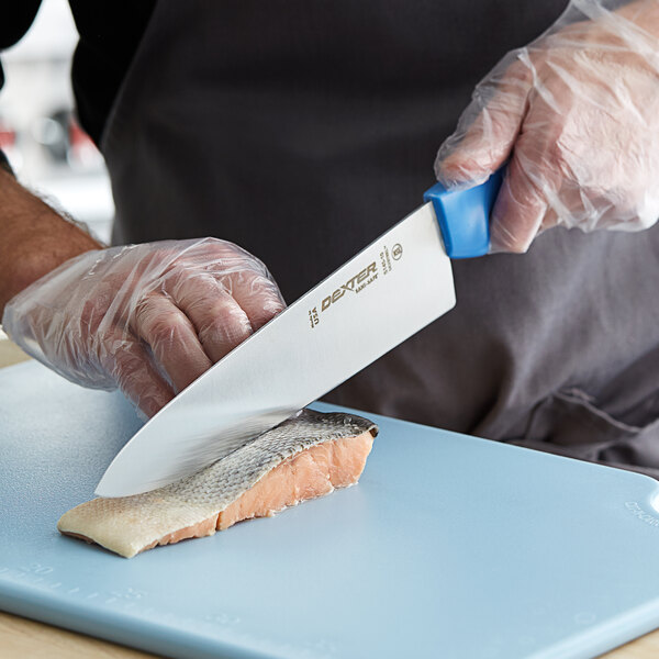 A person in gloves using a Dexter-Russell blue chef knife to cut a piece of fish.