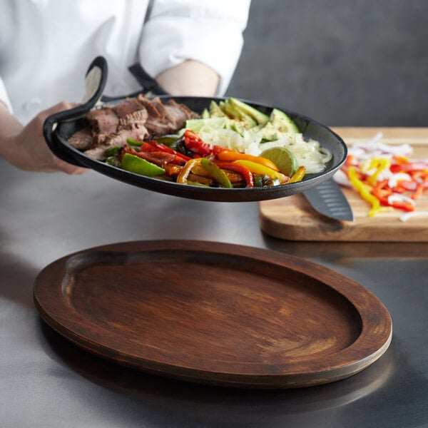 A chef holding a plate of food on a Valor rustic chestnut oval underliner.