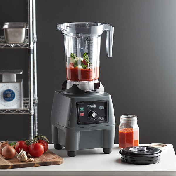 A Waring commercial food blender with a container of red sauce on the counter.