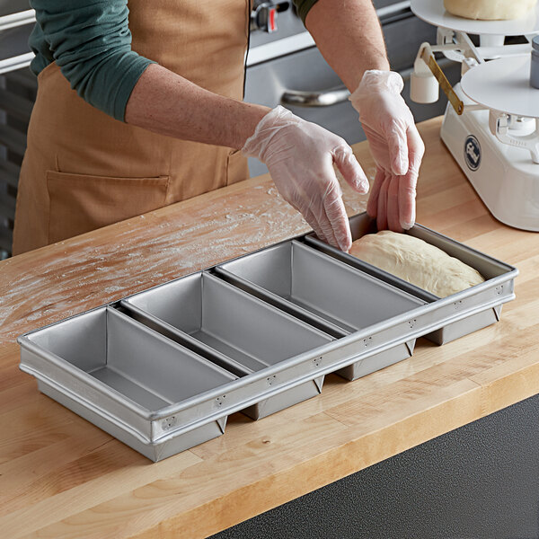 A person wearing gloves puts dough into a Baker's Mark aluminized steel bread loaf pan.