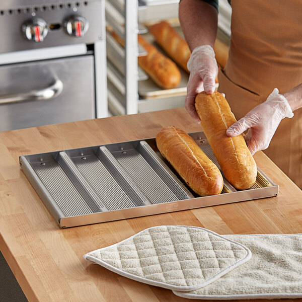 A person holding a loaf of bread on a Baker's Mark sub sandwich roll pan.