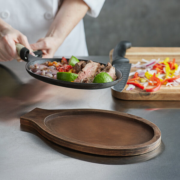 A chef using a Choice oval pine wood underliner with oak finish to serve food from a skillet.