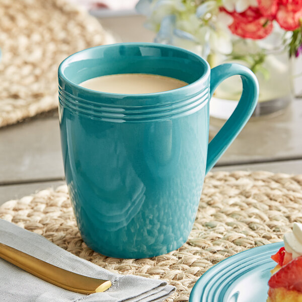 An Acopa Capri Caribbean turquoise stoneware mug filled with a white drink on a table with food and a knife.