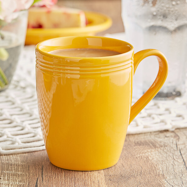 A close-up of a yellow Acopa Capri stoneware mug filled with a yellow liquid on a table with a yellow plate.