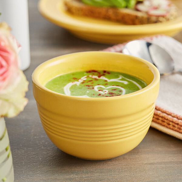 A close-up of a yellow Acopa Capri stoneware bowl filled with green soup on a table.