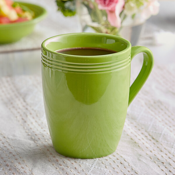 A green Acopa Capri stoneware mug with a handle on a table next to a bowl of food.