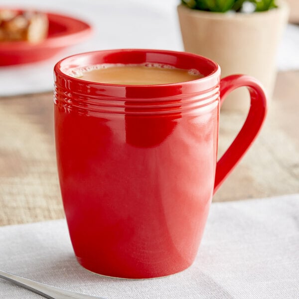 A close-up of an Acopa Capri passion fruit red stoneware mug filled with brown liquid.