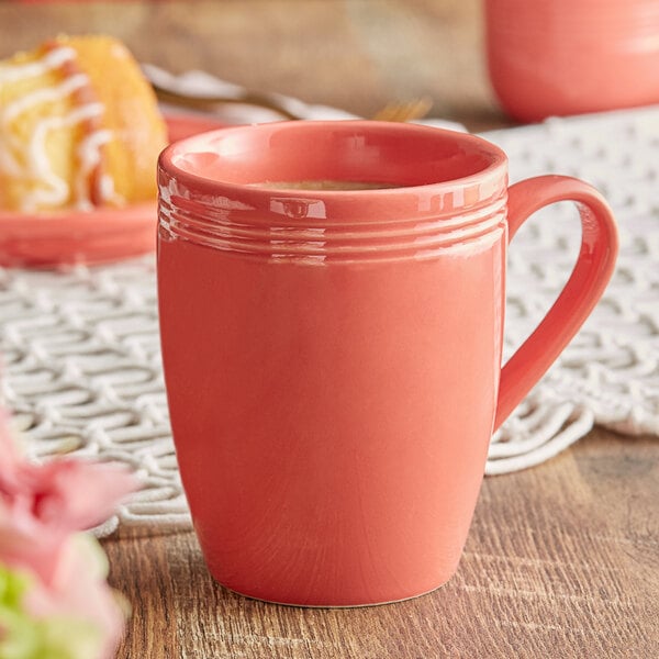 An Acopa Capri coral stoneware mug filled with coffee on a table with pastries.