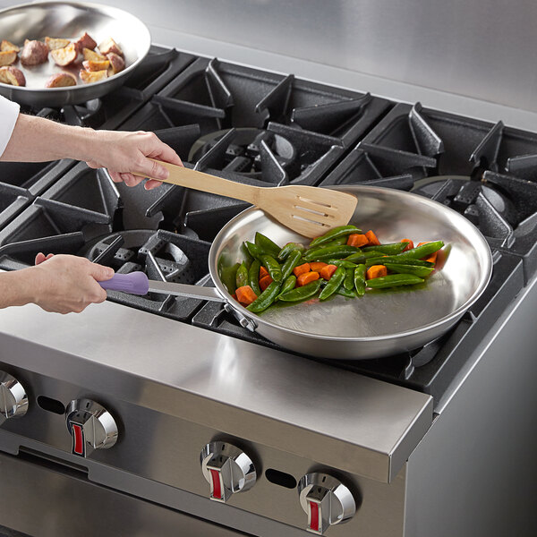 A woman using a Vollrath stainless steel fry pan to cook vegetables.