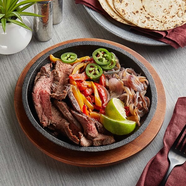 A Valor pre-seasoned cast iron fajita skillet with steak and vegetables on a wood surface.