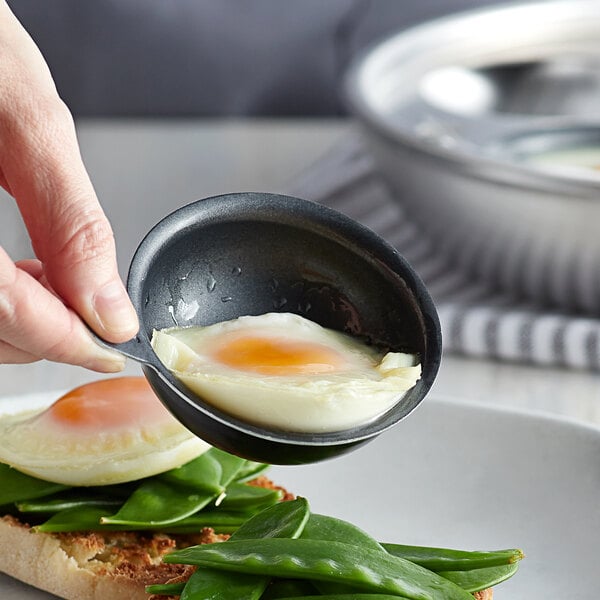 A close-up of a Vollrath aluminum egg poacher cup with a cooked egg inside.