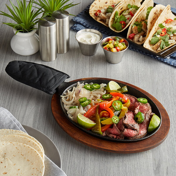 A Valor oval cast iron fajita skillet with steak and vegetables on a wood table.