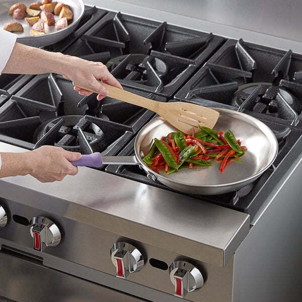 A woman cooking vegetables in a Vollrath stainless steel fry pan on a stove.