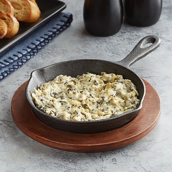 A Valor pre-seasoned cast iron skillet with food on a wooden plate.