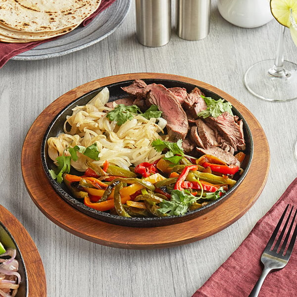 A Valor pre-seasoned cast iron fajita skillet with meat and vegetables on a wood surface.