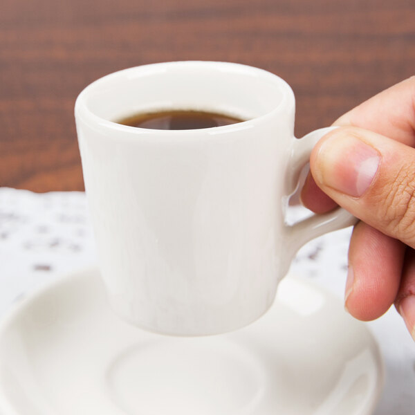 A hand holding a Tuxton white china espresso cup of coffee.