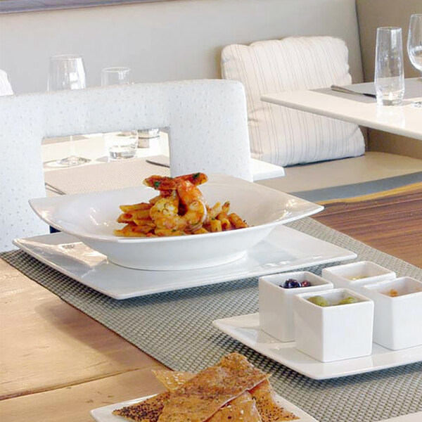 A white table set with a white Front of the House square bowl filled with food.