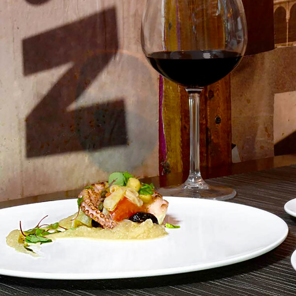 A white Front of the House porcelain plate with food on it next to a glass of wine.