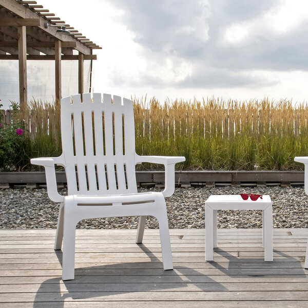 Two white Grosfillex resin Adirondack chairs on a wood deck.