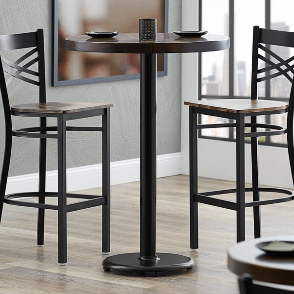 A Lancaster Table & Seating bar height table with a glass top on a cast iron table base.