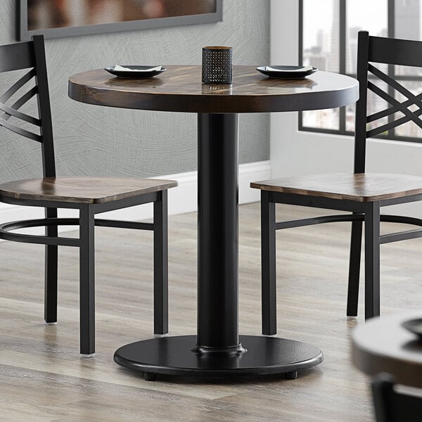 A Lancaster Table & Seating cast iron table base with self-leveling feet on a round table in a restaurant with two chairs.