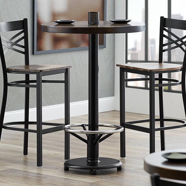 A Lancaster Table & Seating cast iron bar height table base with a foot rest and table equalizers on a table in a restaurant dining area.