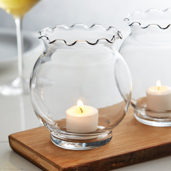 Two Anchor Hocking glass votives with candles on a table.