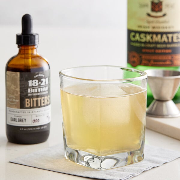 A glass of whiskey next to a bottle of 18.21 Earl Grey Bitters.