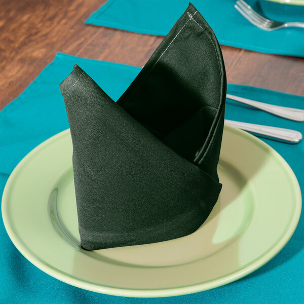 A folded hunter green Intedge cloth napkin on a plate with silverware.