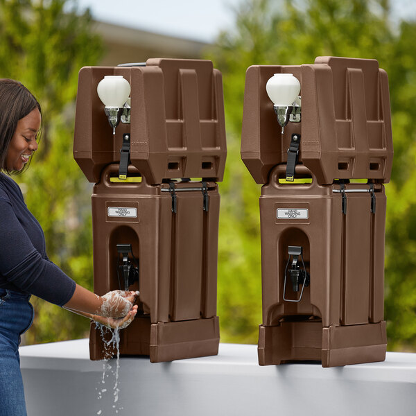 A woman washing her hands with a brown plastic Cambro handwash station.