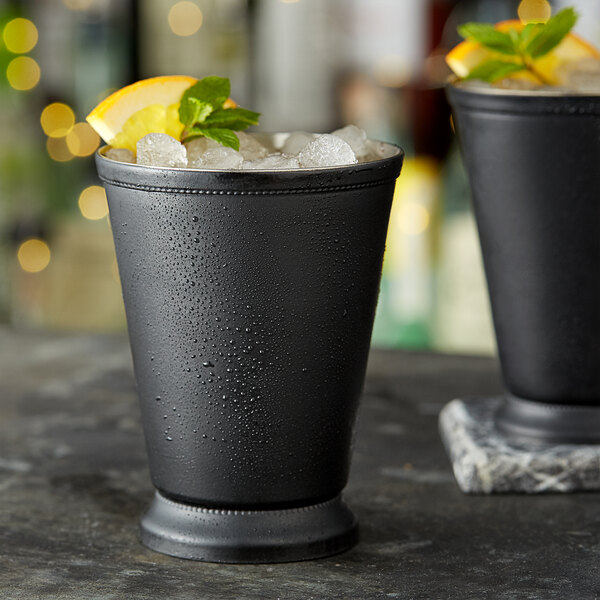 Two Acopa matte black mint julep cups with ice and lemon slices.