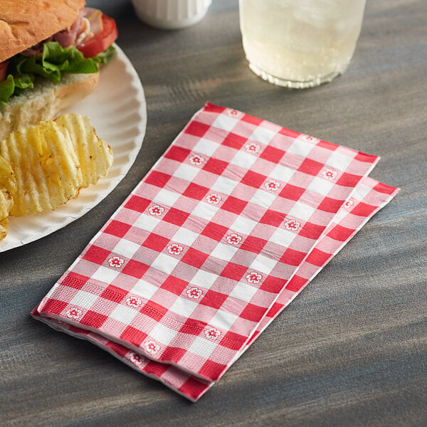 A plate of food with a sandwich and a red and white checkered Choice dinner napkin.