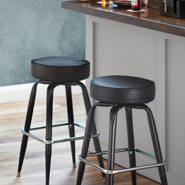 Two black Lancaster Table & Seating bar stool seats on metal bar stools.