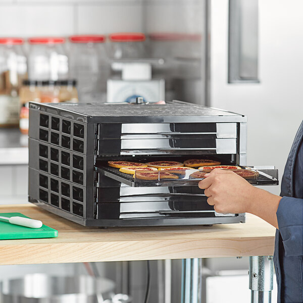 A person holding a Backyard Pro Butcher Series food dehydrator tray full of food.