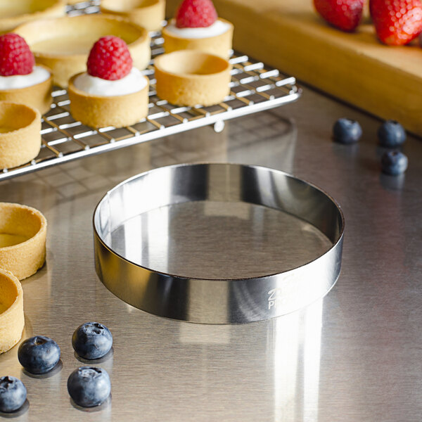 A Fat Daddio's stainless steel circular tart ring on a table with small tarts topped with raspberries.