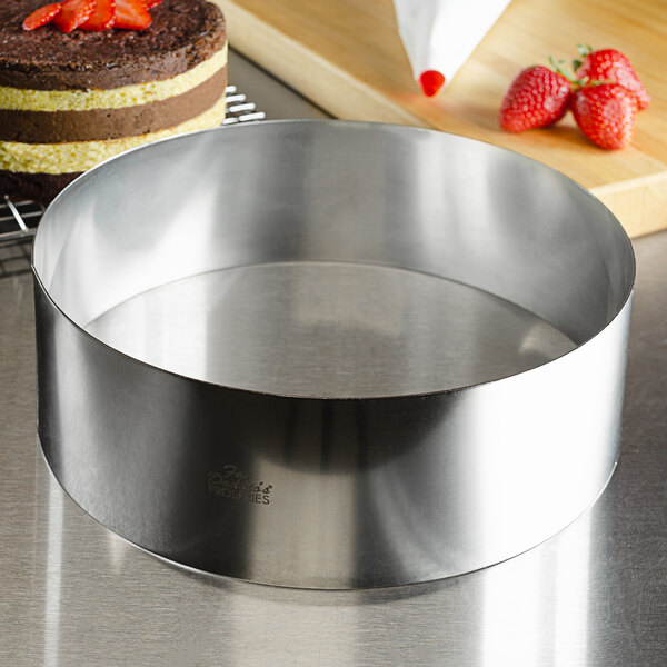 A stainless steel round cake ring filled with a round cake on a table.