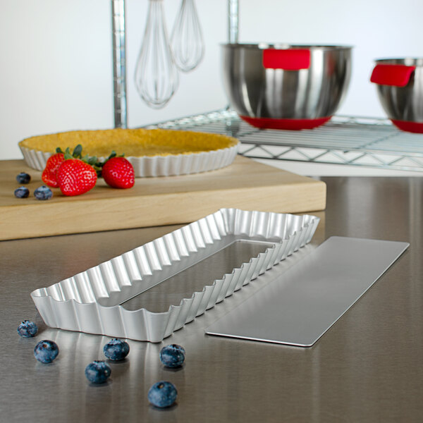 A Fat Daddio's rectangular metal quiche pan with a wavy edge and removable tray on a counter.