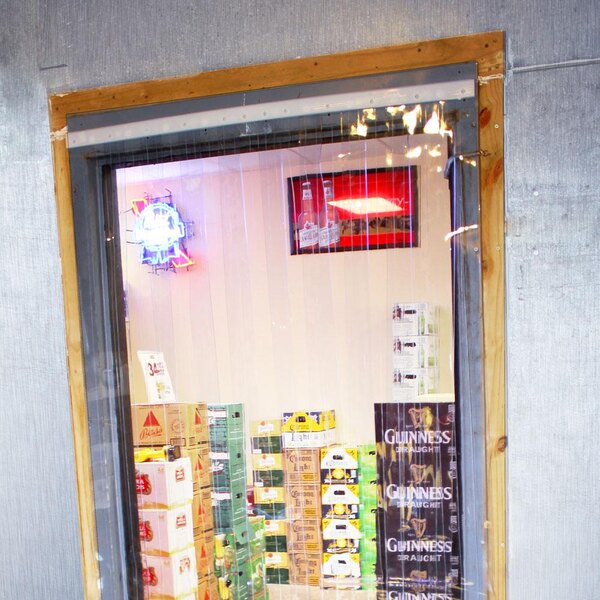 A storefront with a Curtron strip door with boxes of beer inside.