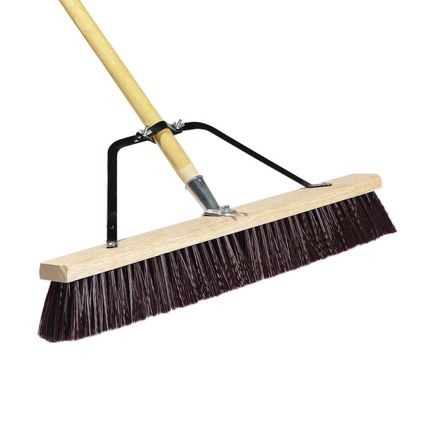 A Carlisle commercial push broom with a wooden handle and black bristles.