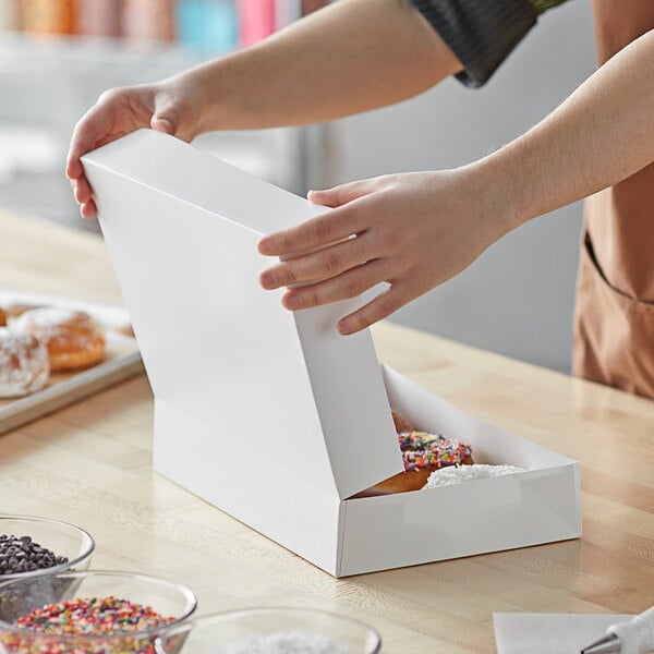 A hand opening a Baker's Mark white box of doughnuts.