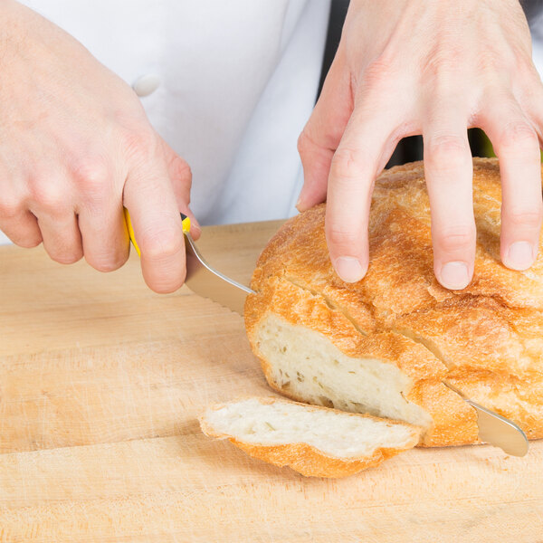 A person using a yellow Mercer Culinary Millennia Colors bread knife to cut a loaf of bread.