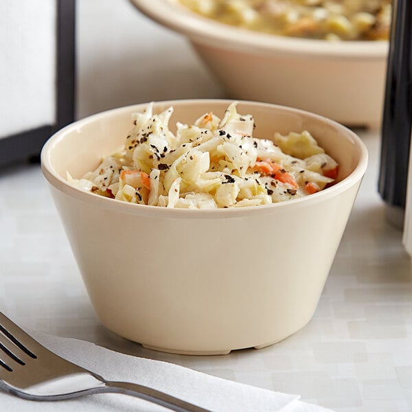 An Acopa tan melamine bowl filled with coleslaw with a fork.