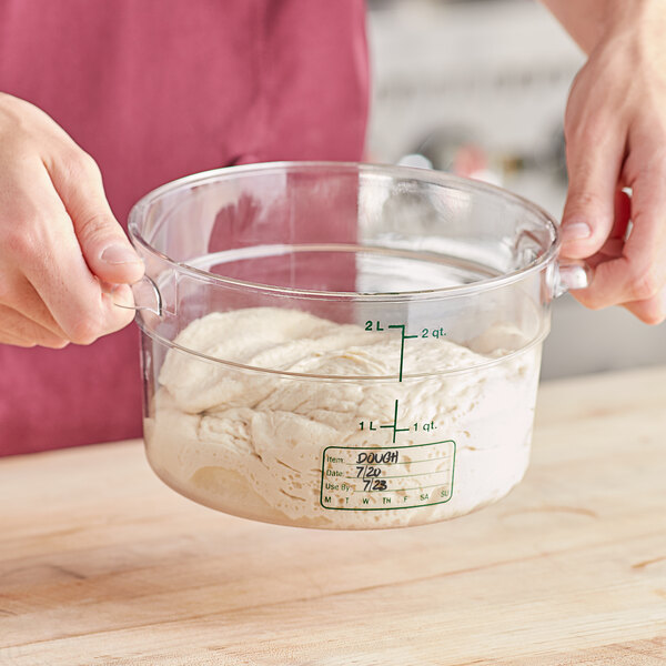 A person holding a Vigor round food storage container with dough in a measuring cup.
