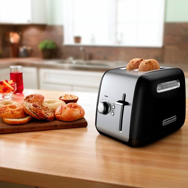 A black and silver KitchenAid toaster on a counter with a plate of bagels and a sandwich.