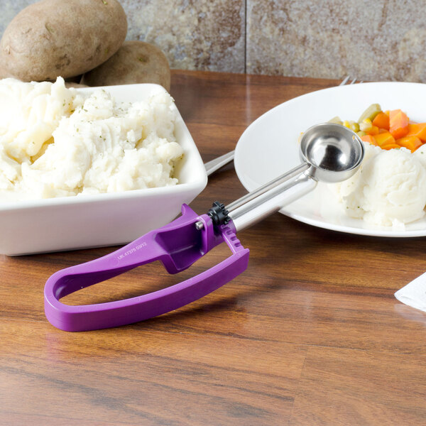 A Vollrath Jacob's Pride purple ice cream scoop with a metal bowl on a metal handle next to a bowl of mashed potatoes.