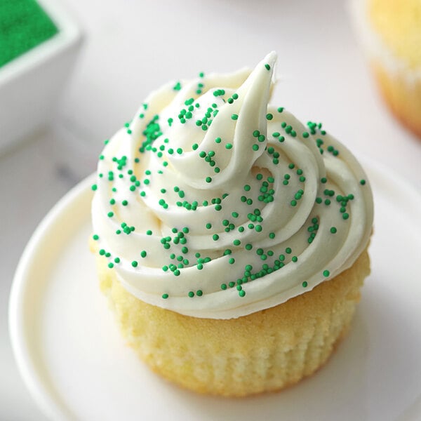 A cupcake with white frosting and green nonpareils.