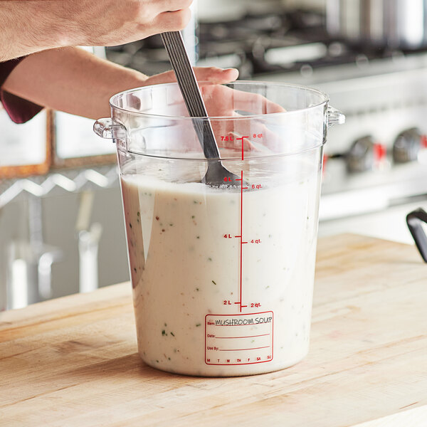 A person pouring a white liquid from a measuring cup into a Vigor food storage container on a counter.