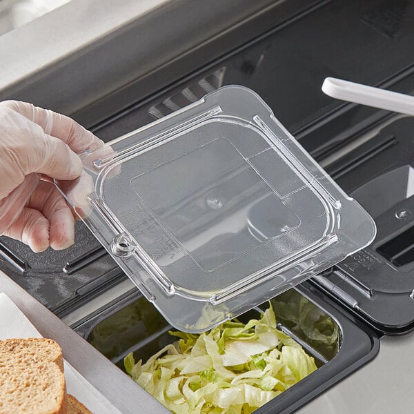 A person's gloved hand using a Vigor clear plastic lid to cover food in a clear plastic container.